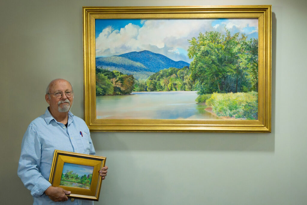 Artist Andrei Kushnir Gifts Original Oil Paintings To Shenandoah University Artist Andrei Kushnir poses with a large framed oil painting of the Shenandoah River while holding another small painting of the Shenandoah Valley landscape.