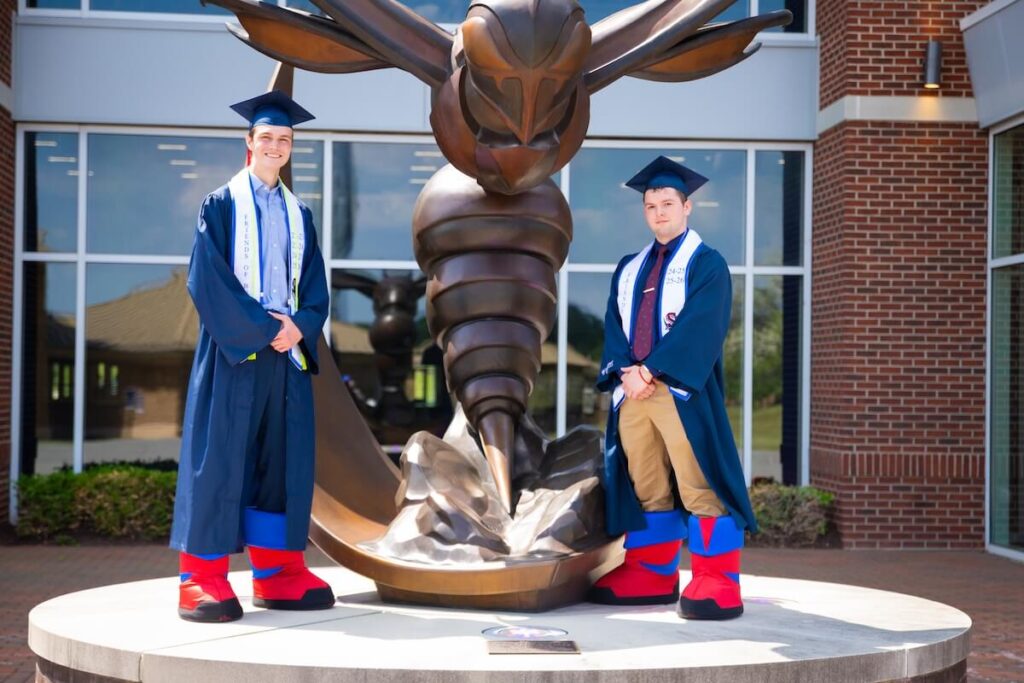Shenandoah students pose in graduation regalia and Buzzy mascot feet.